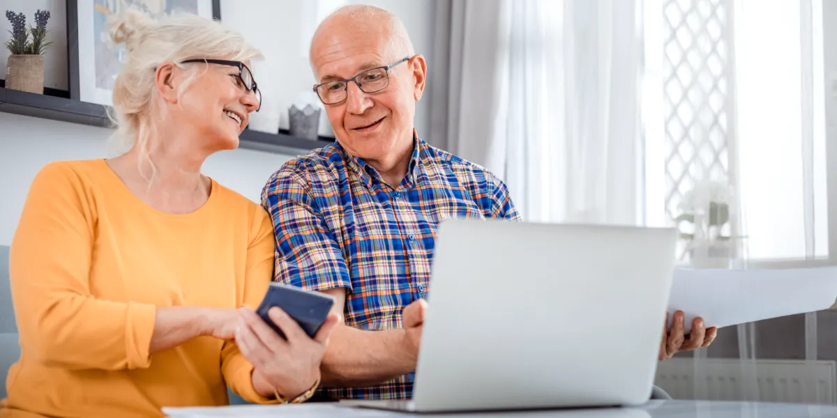 elderly couple looking at calculator while sitting in front of computer