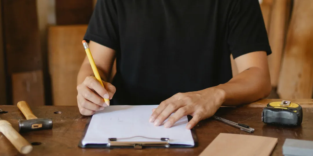 man drawing on piece of paper with construction utensils on table