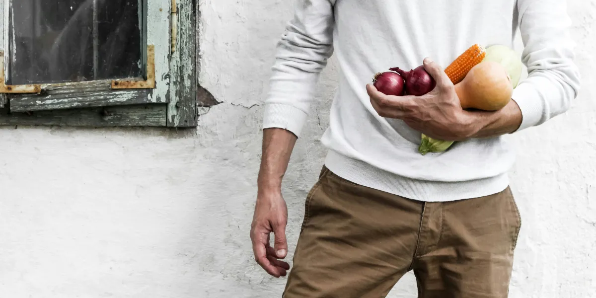 man holding vegetables leaning against a house