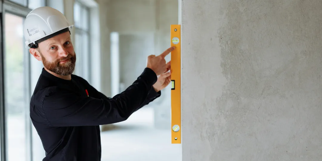 man holding yellow spirit level against wall