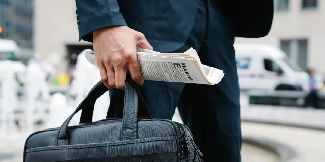 man in suit holding laptop bag and newspaper