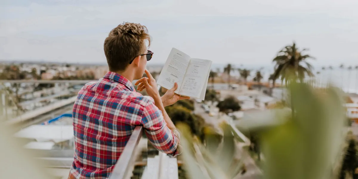 man reading book while standing on balcony overlooking the city