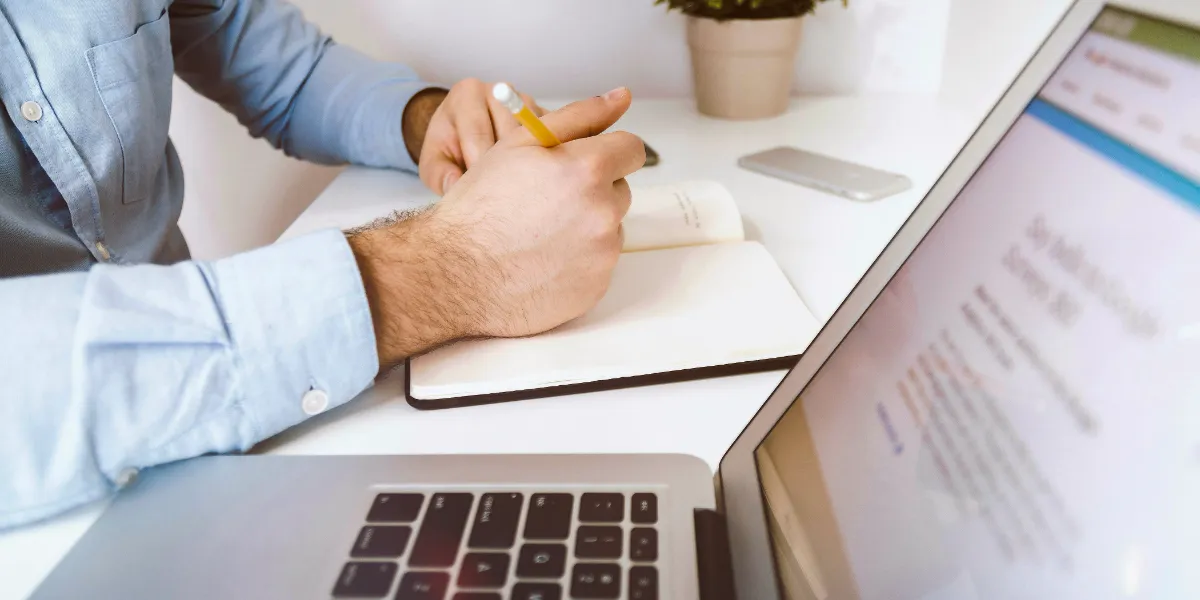 man taking notes with computer on desk