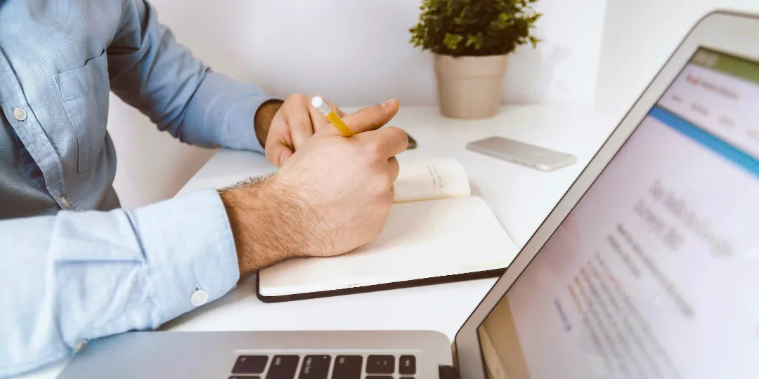 man taking notes with laptop on desk