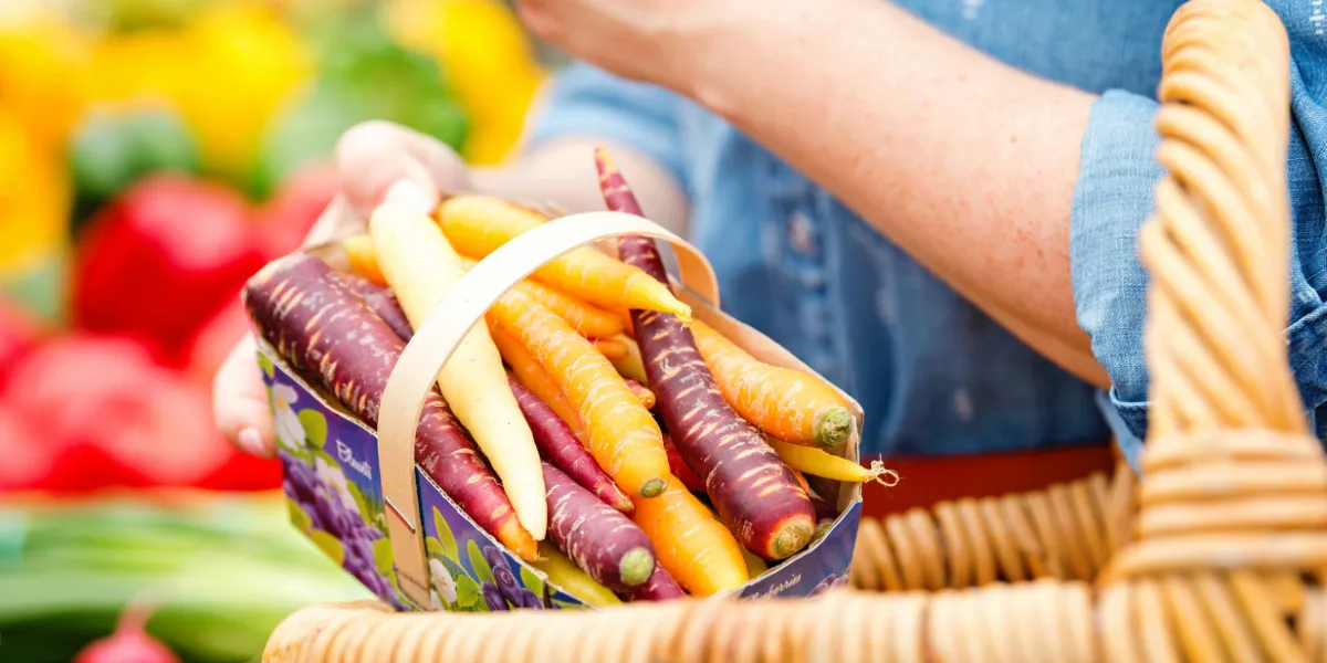 person putting a pack of carrots in a basket