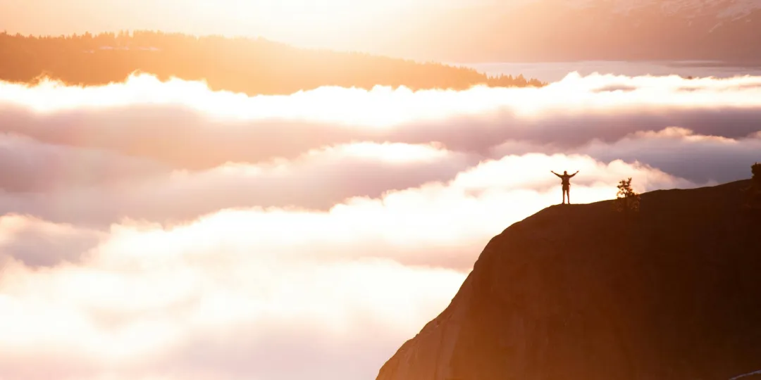 person standing on a mountain above the clouds