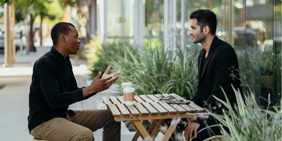 two men talking while drinking coffee at a cafe