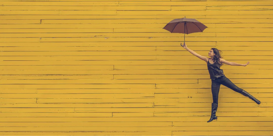 woman holding an umbrella in front of a yellow wall