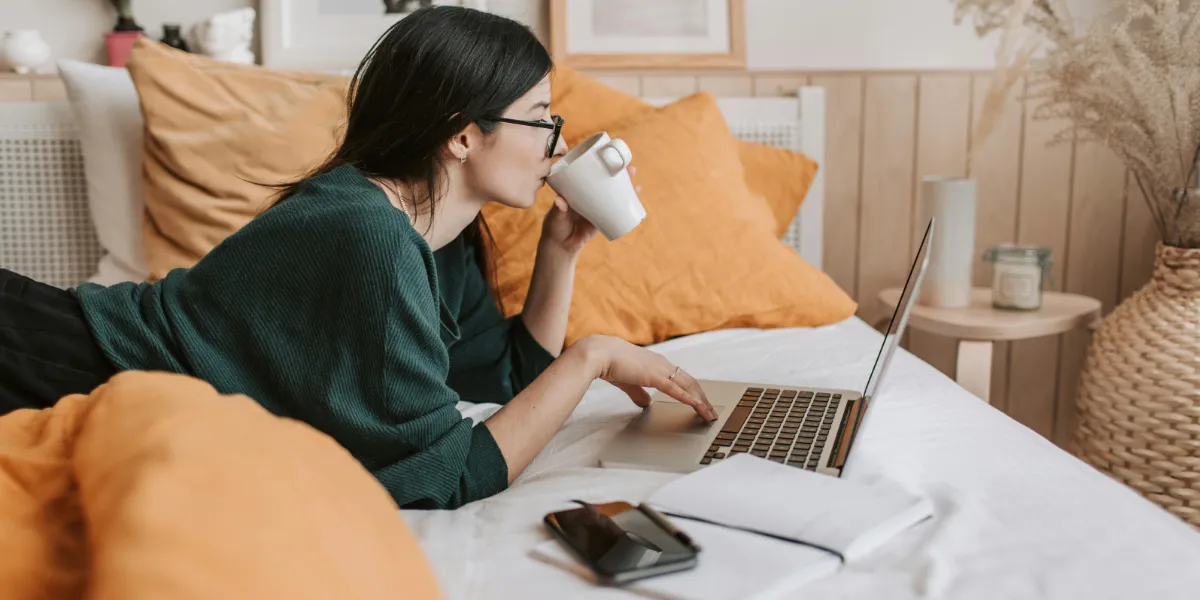 woman laying on bed with computer sipping on cup