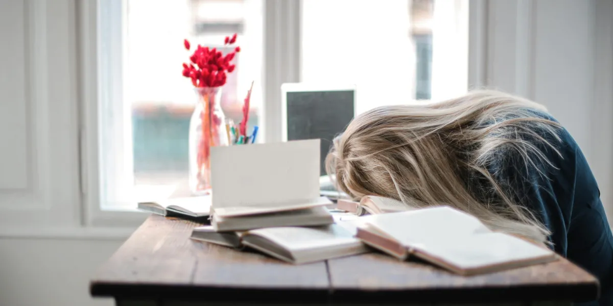 woman laying with head on desk surrounded by books