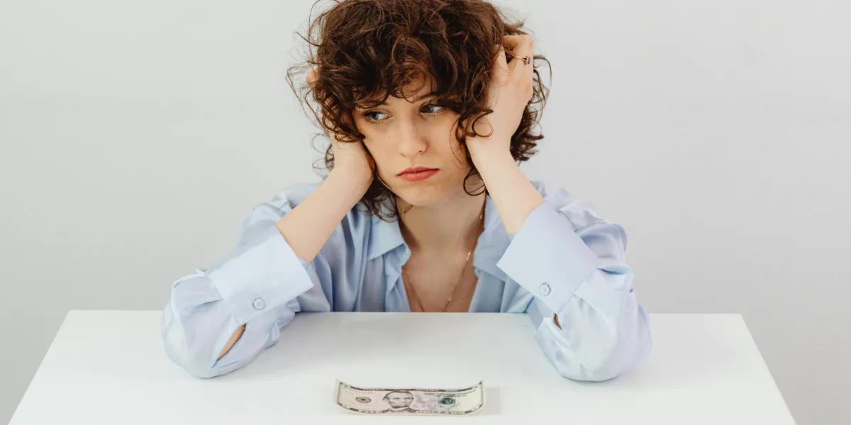 woman looking frustrated with dollar bill in front of her