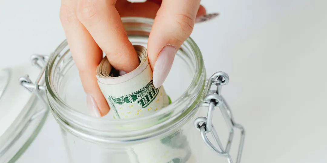 woman putting money in glass jar