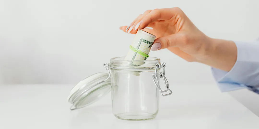 woman putting money roll in glas jar