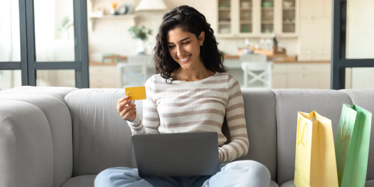 woman sitting on a sofa holding a credit card while looking at a computer