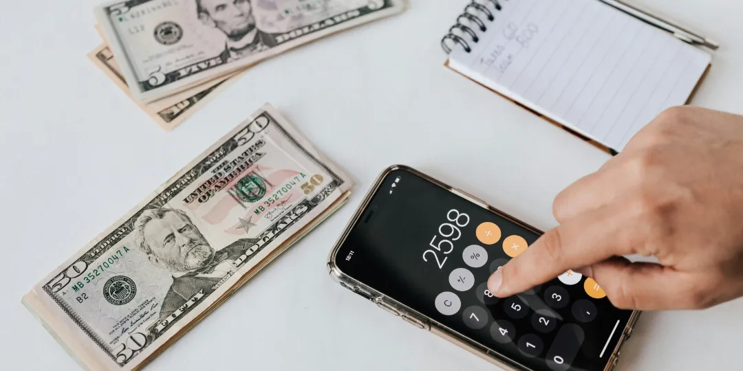 woman using the calculator app on her phone with money on the table