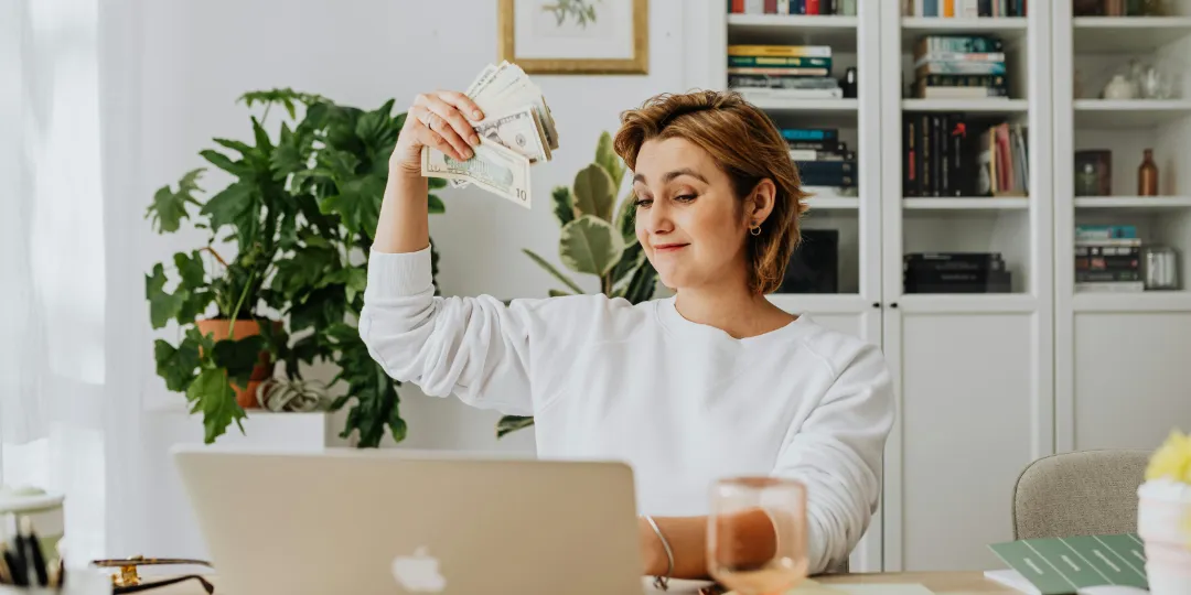 woman waving money while looking at computer